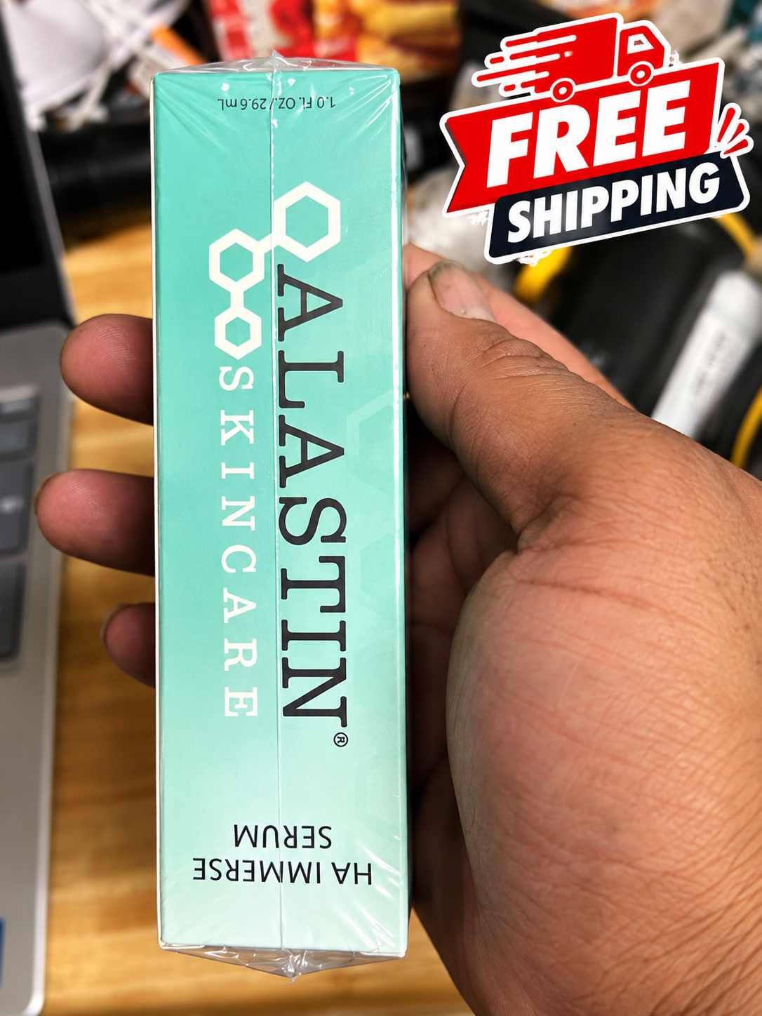 A hand holding a mint green box of Alastin Skincare HA Immersive Serum, with a 'FREE SHIPPING' graphic overlay in the top right corner.
