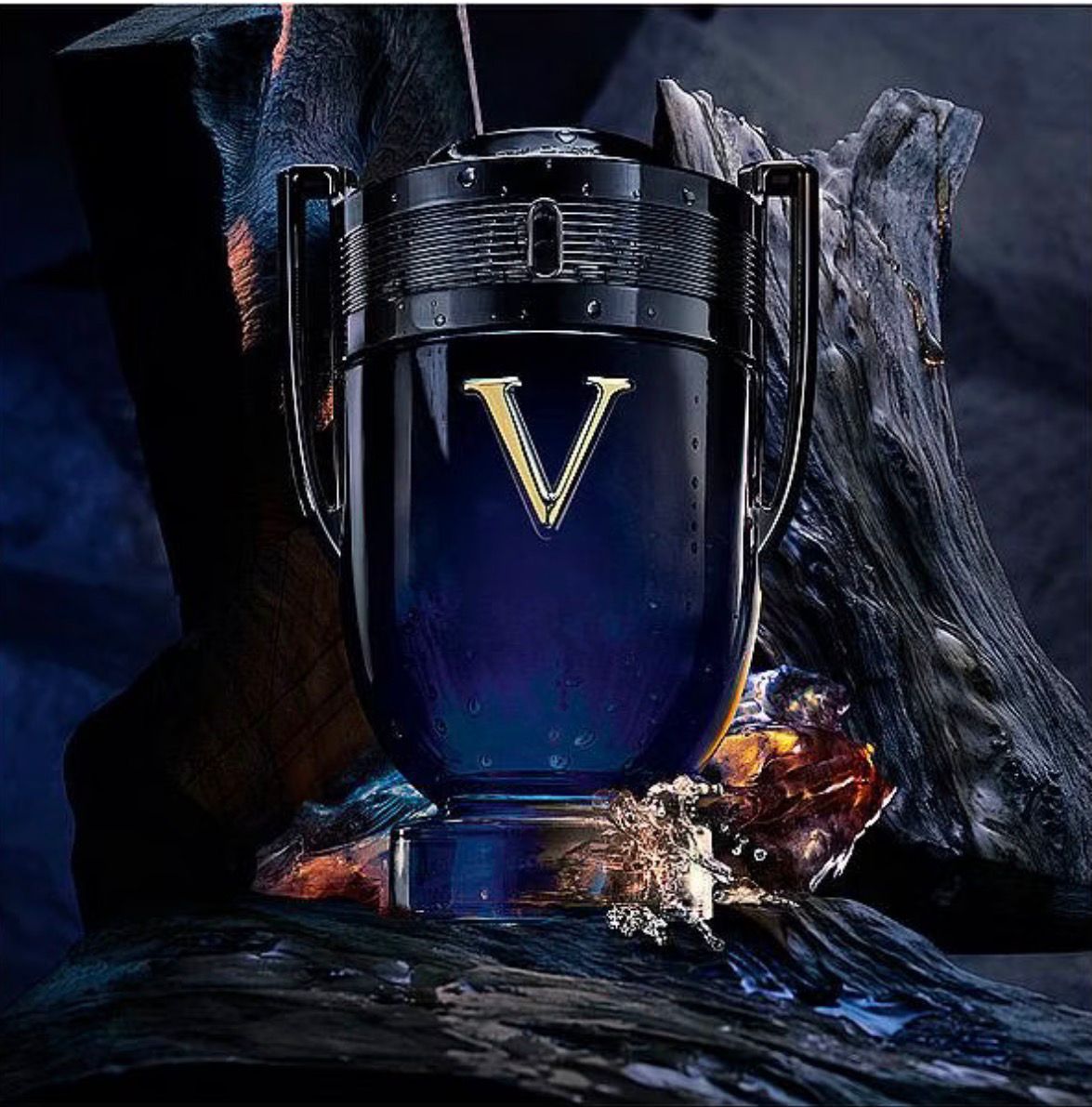 A dark blue and black perfume bottle with a large gold 'V' logo, styled on a dark textured surface with dramatic lighting and a blurred background.